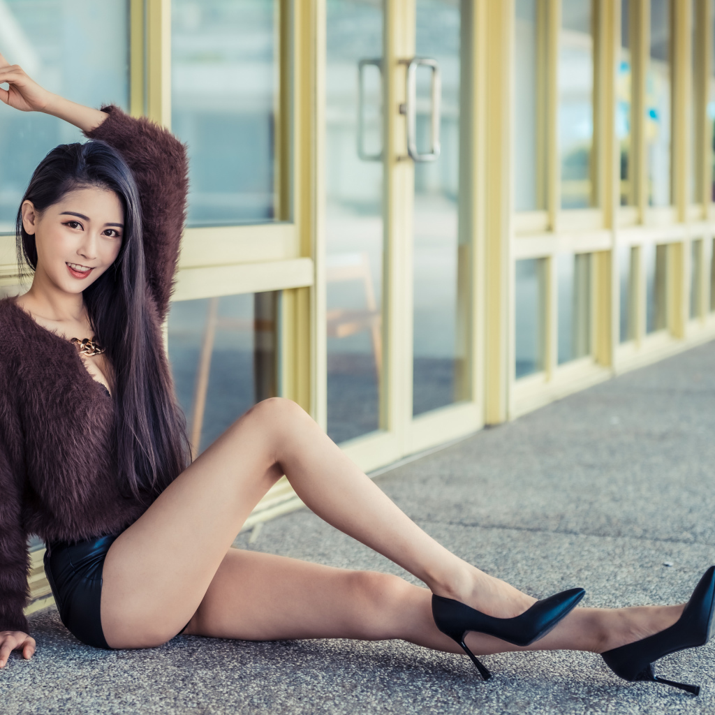 Девушка в свитере сидит у стеклянной стены 