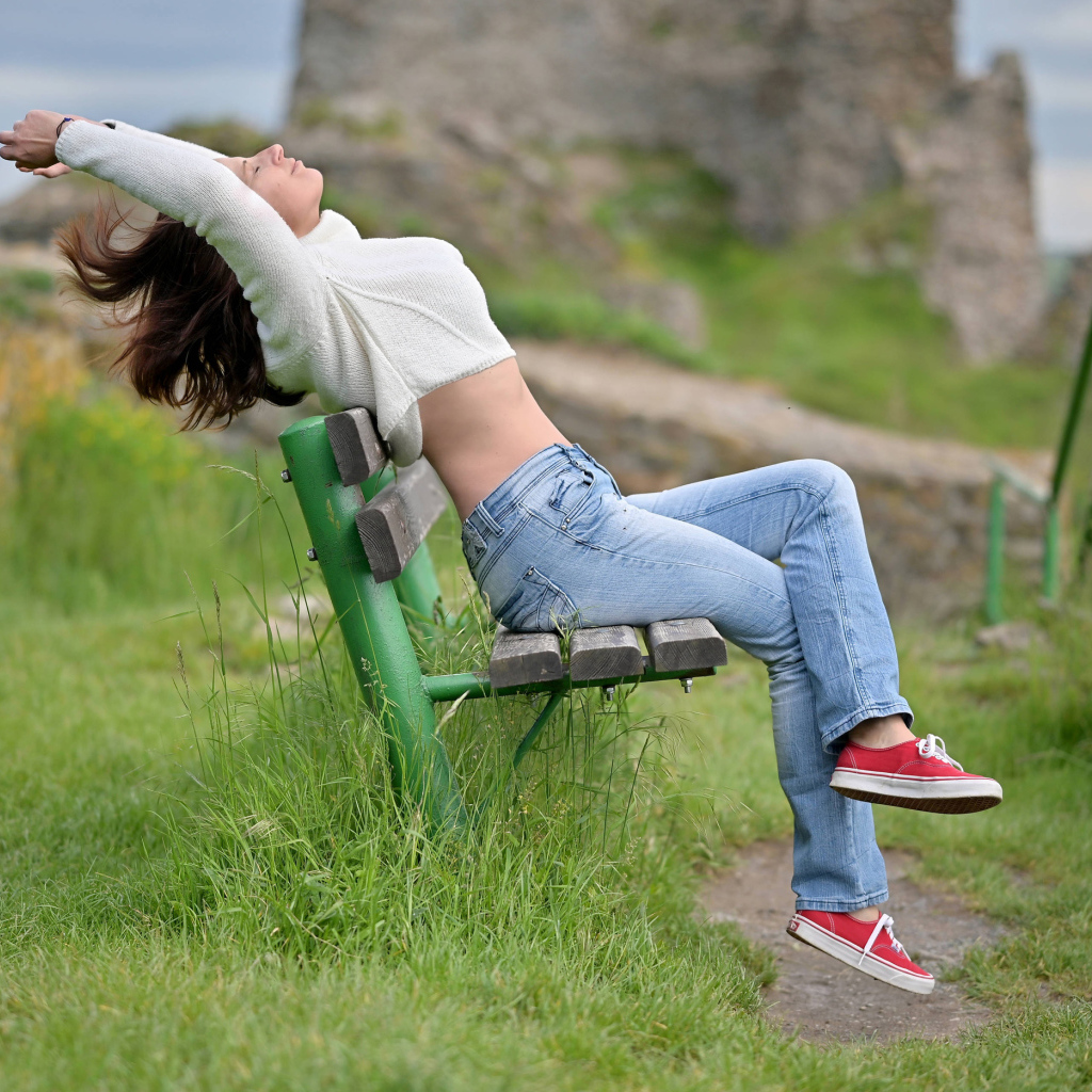 Девушка в синих джинсах сидит на лавке 