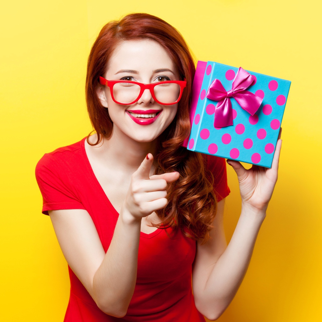 Девушка в очках с подарком в руке на желтом фоне