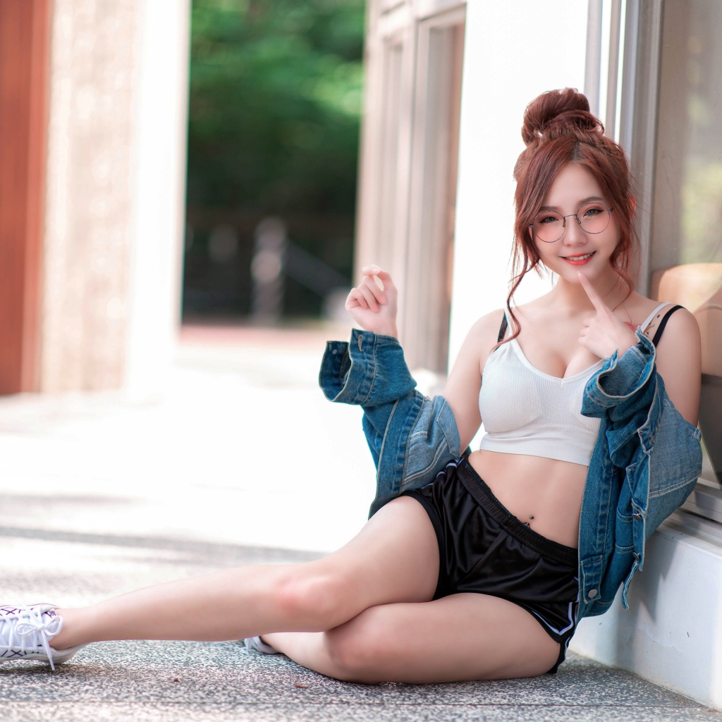 Молодая девушка азиатка в джинсовой куртке сидит у окна