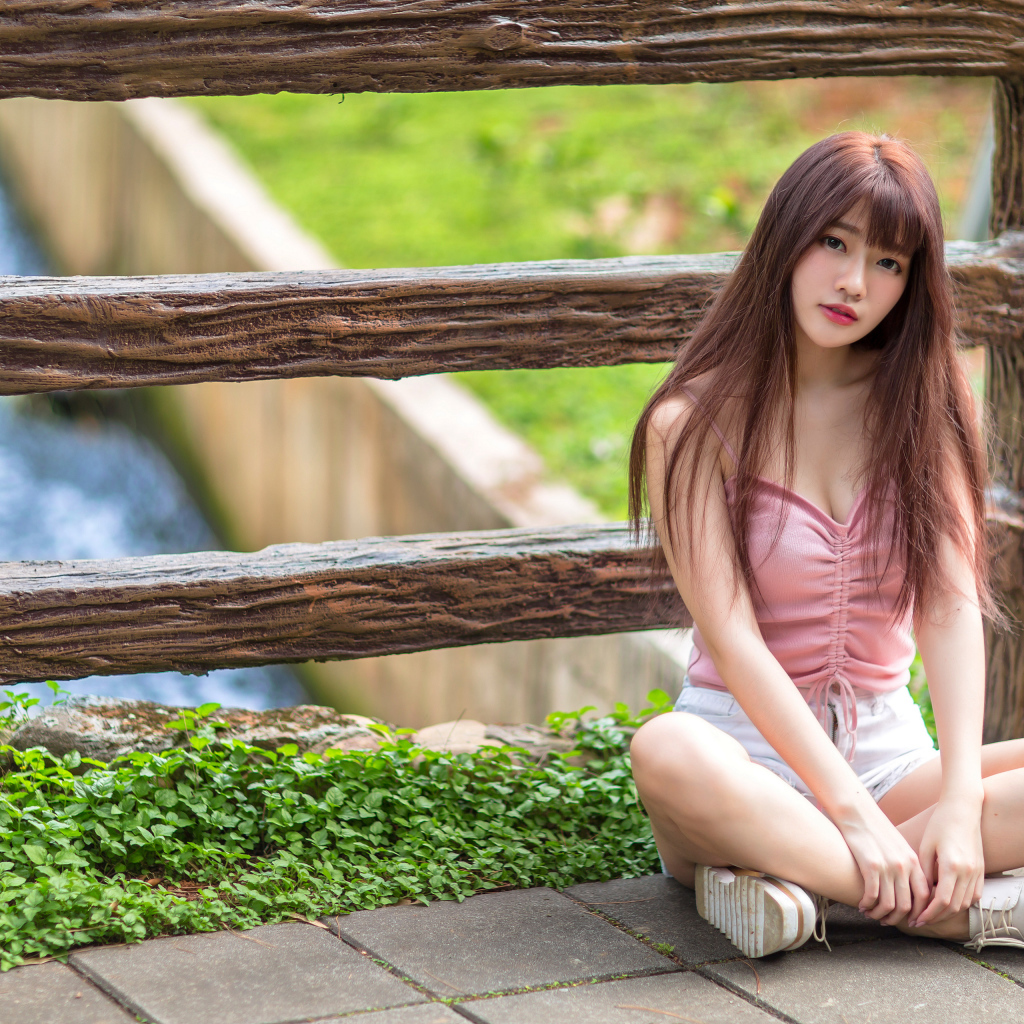 Длинноволосая азиатка сидит у забора 