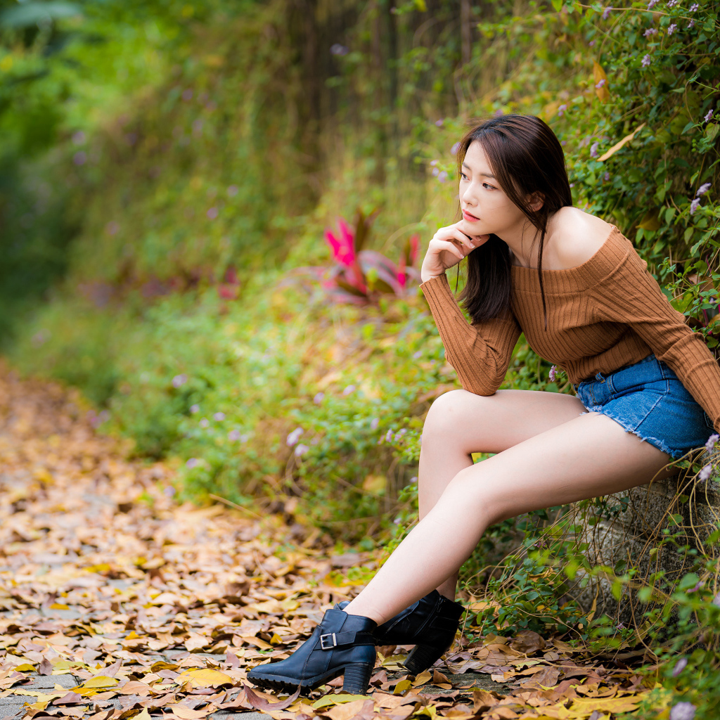 Задумчивая азиатка сидит в парке осенью 