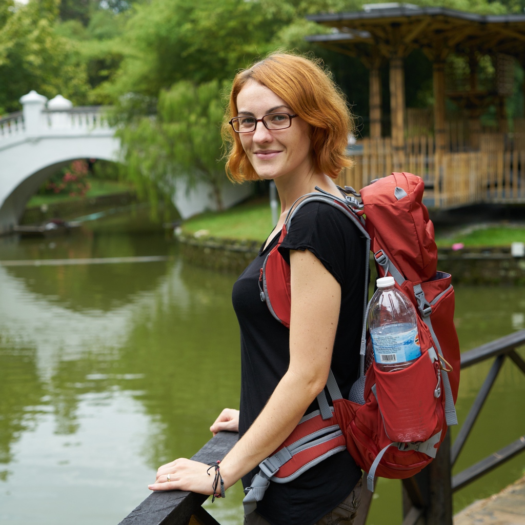 Рыжеволосая девушка с рюкзаком у пруда 