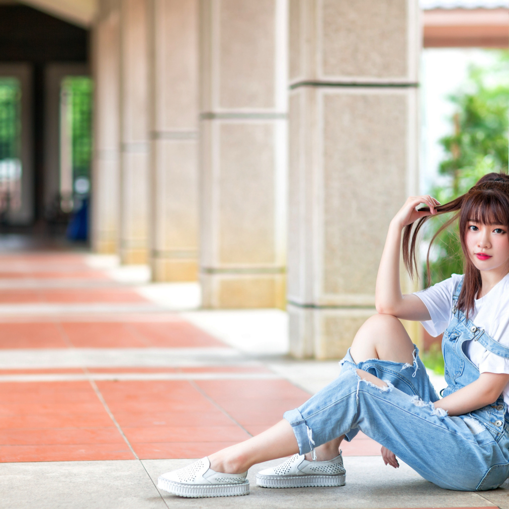 Грустная девушка азиатка сидит у колонны