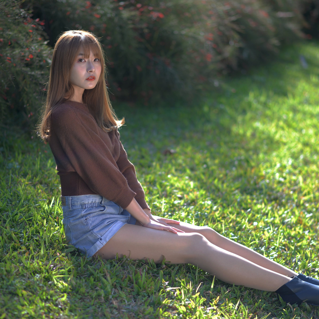 Грустная девушка азиатка сидит на зеленой траве 