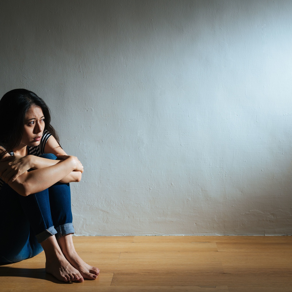 Испуганная девушка азиатка сидит у стены