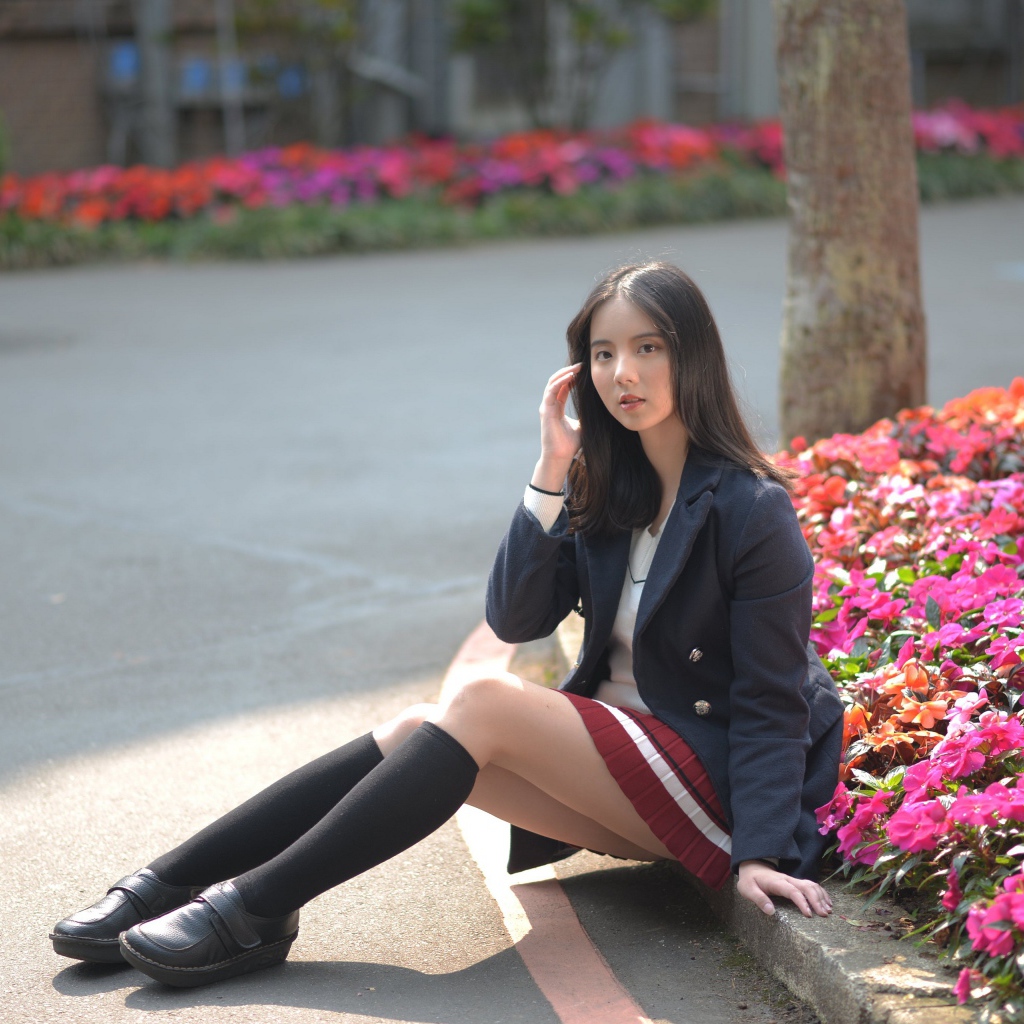 Девушка школьница сидит на земле у клумбы 