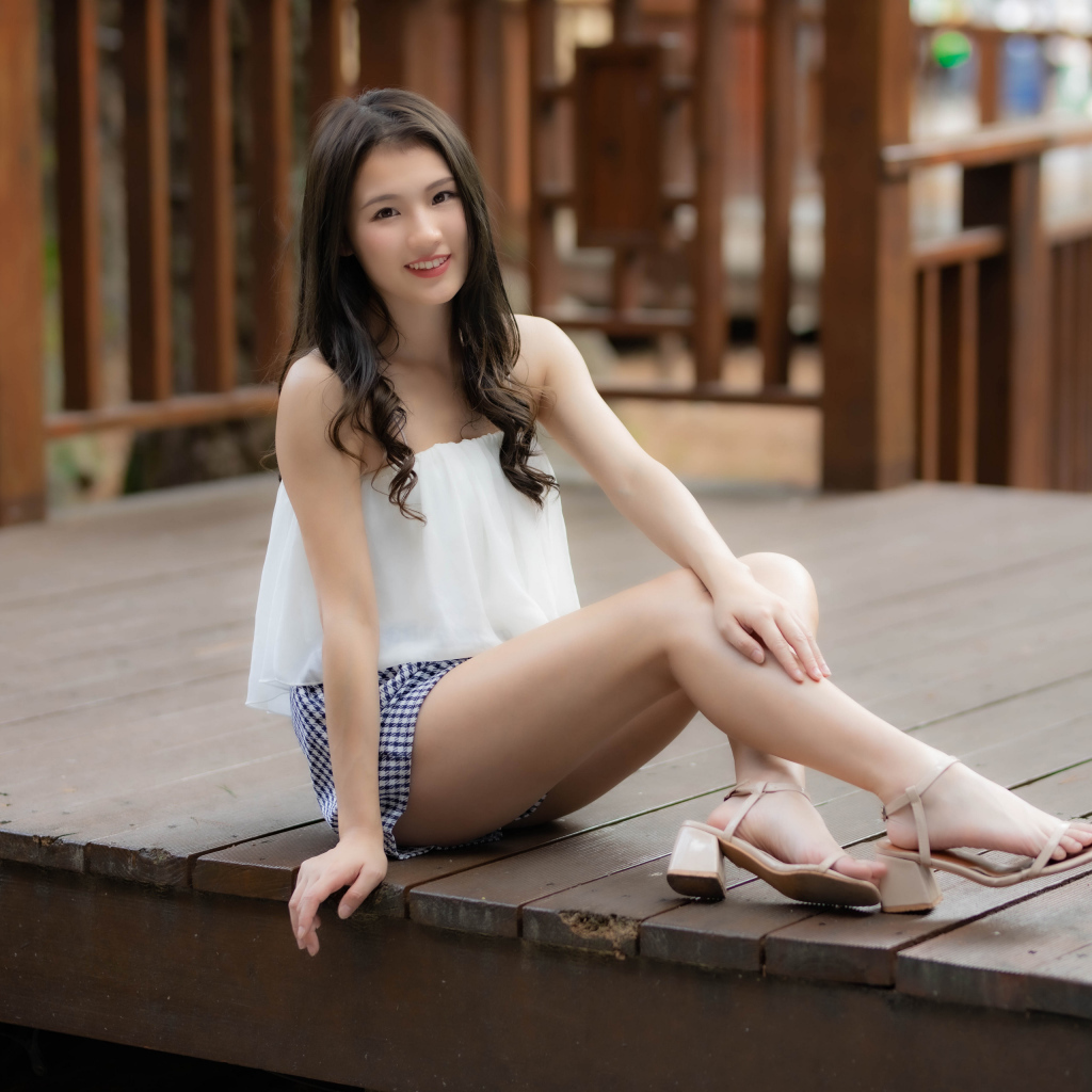 Улыбающаяся девушка азиатка сидит на мосту 