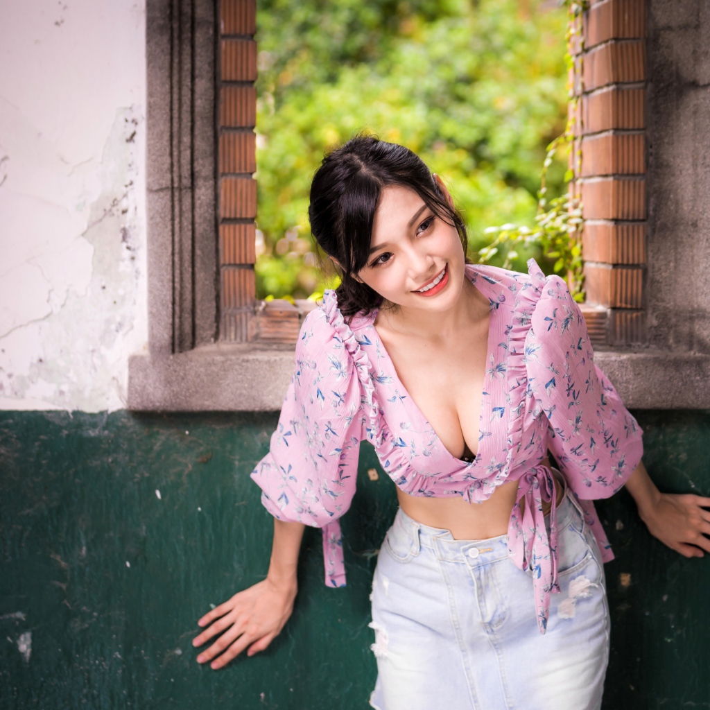 Улыбающаяся девушка азиатка стоит у окна 