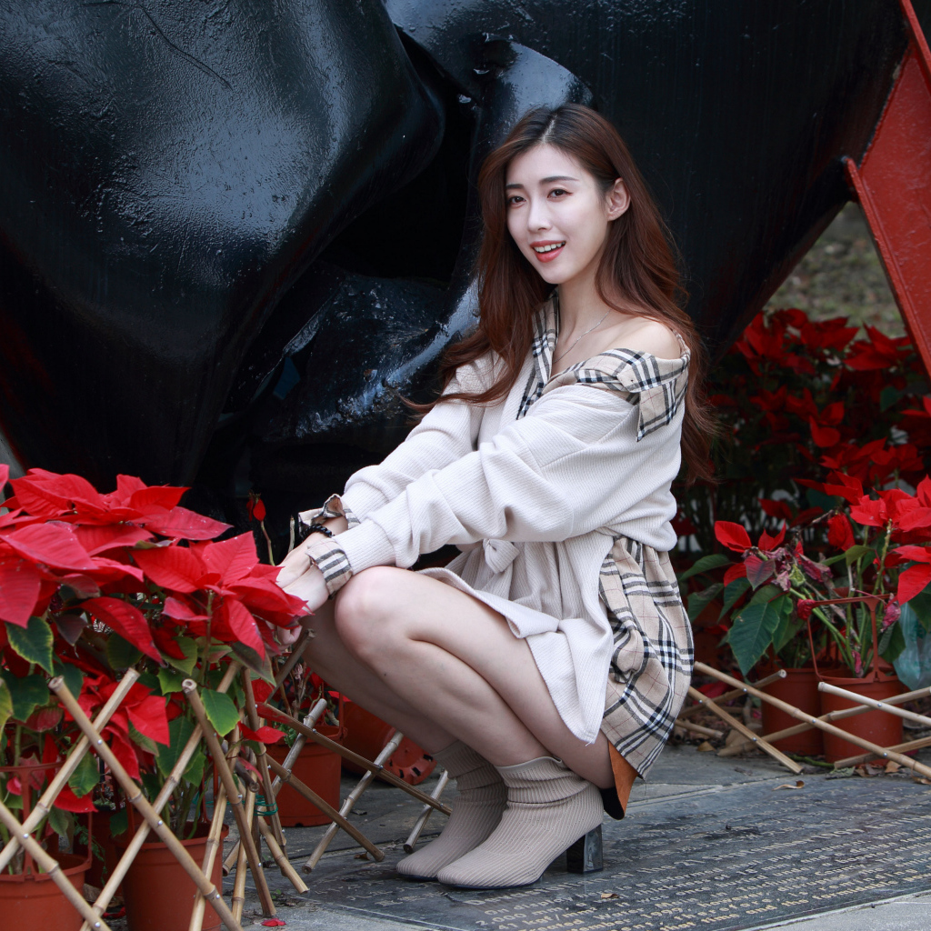 Улыбающаяся азиатка сидит у красных цветов 