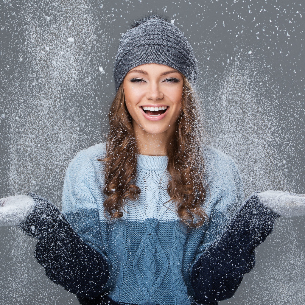 Улыбающаяся девушка ловит снег руками на сером фоне