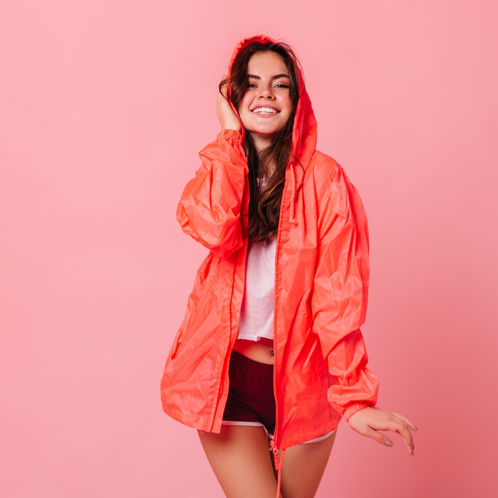 Улыбающаяся девушка в плаще на розовом фоне