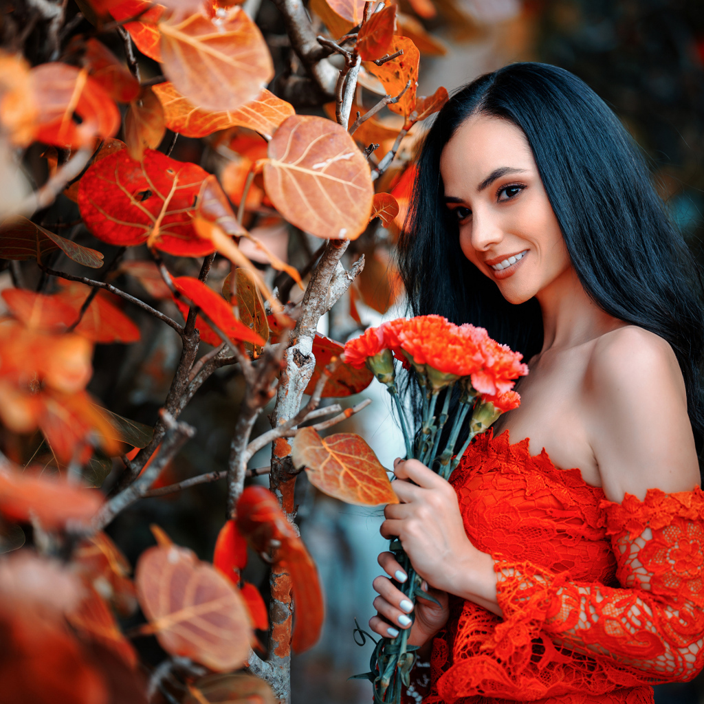 Улыбающаяся девушка с букетом гвоздик у стены с осенними листьями