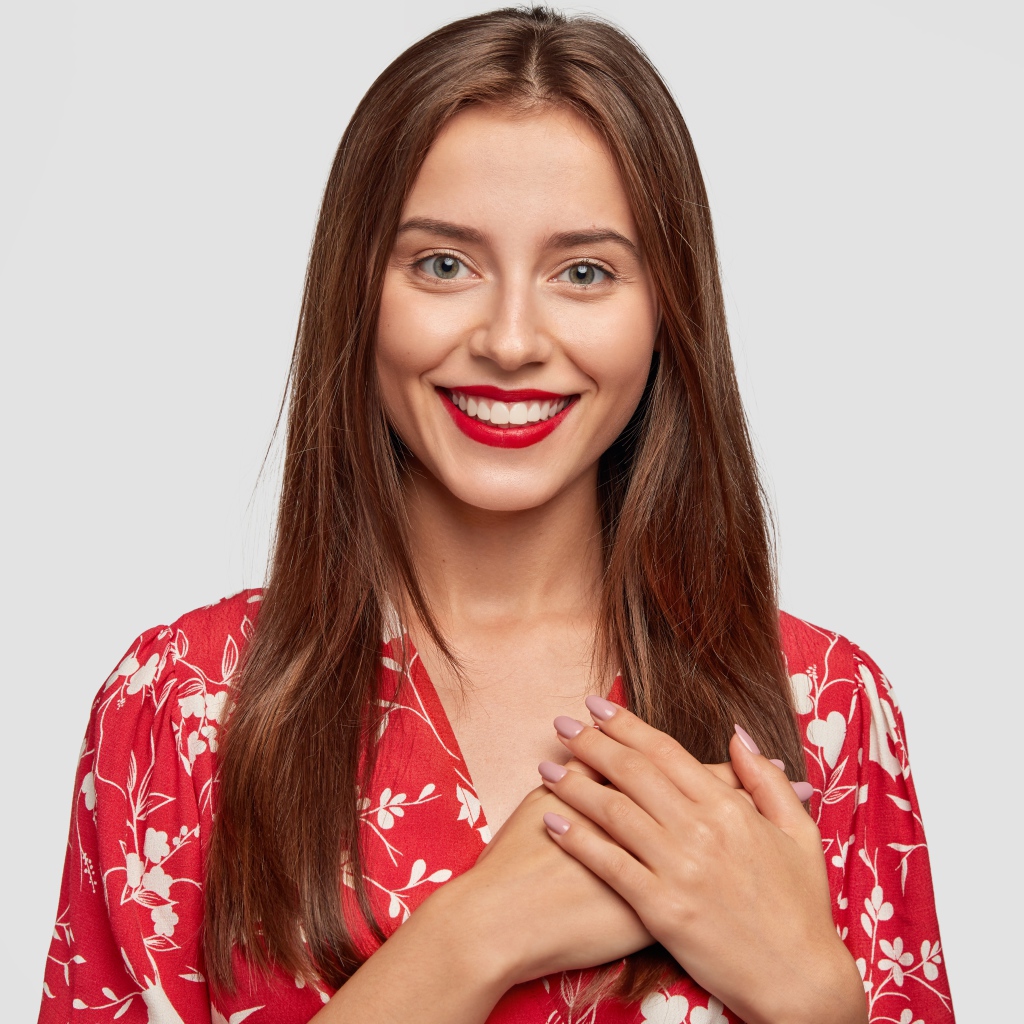 Улыбающаяся девушка с руками на сердце на сером фоне