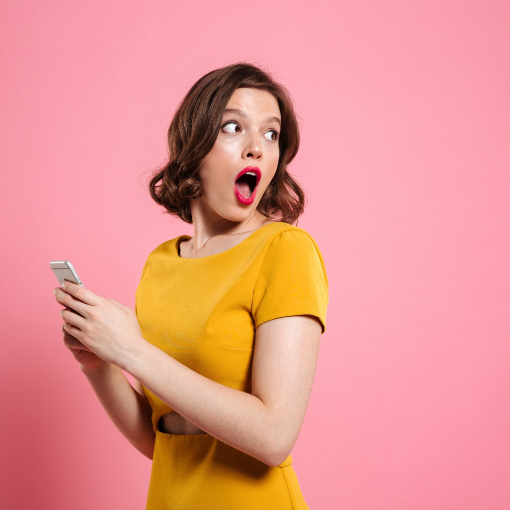 Удивленная девушка с телефоном в руках на розовом фоне