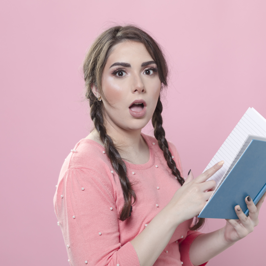 Удивленная девушка с книгой на розовом фоне