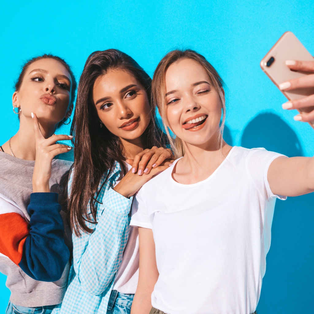 Три подруги делают селфи на голубом фоне