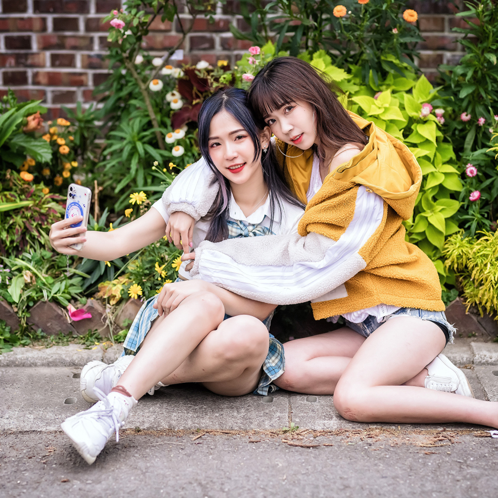 Две девушки азиатки сидят у стены с цветами 