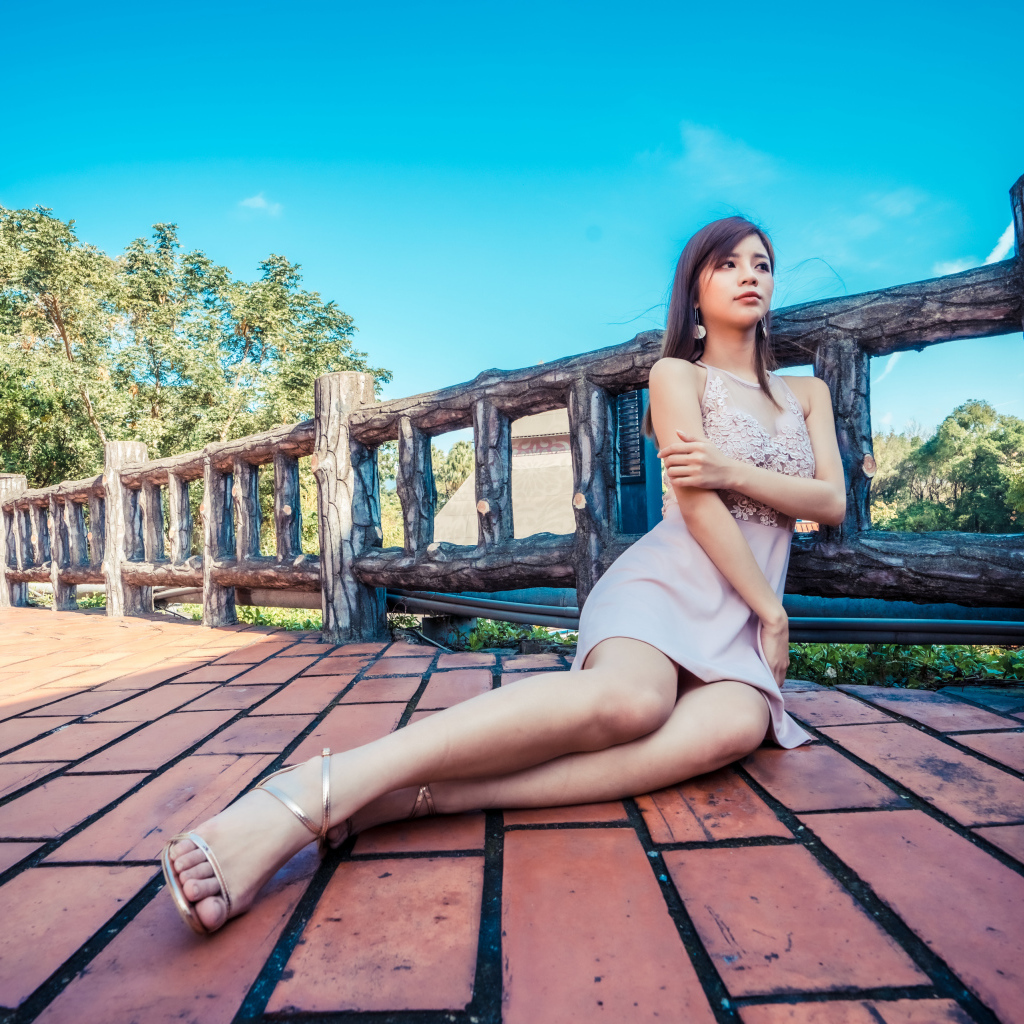 Молодая красивая азиатка сидит  на полу у забора