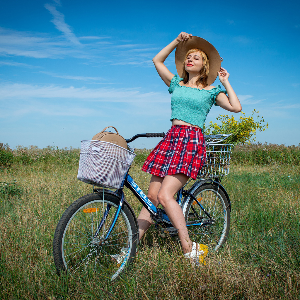 Молодая девушка на велосипеде на поле под голубым небом 