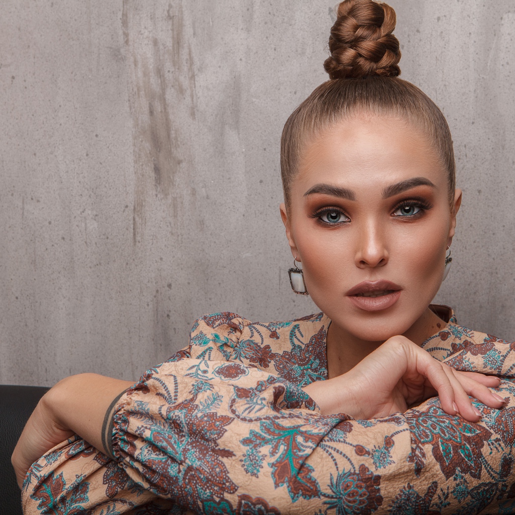 Молодая девушка с прической на голове на фоне стены