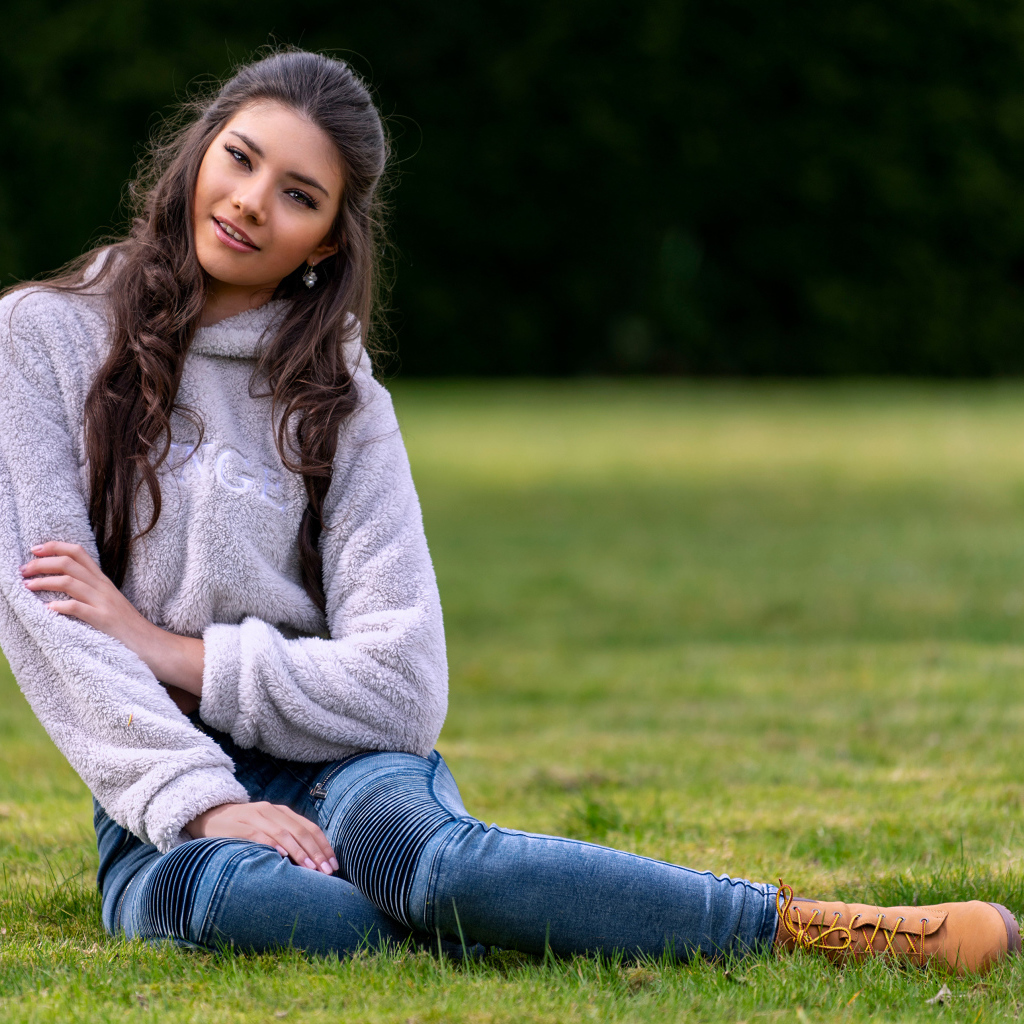 Молодая длинноволосая девушка сидит на траве 