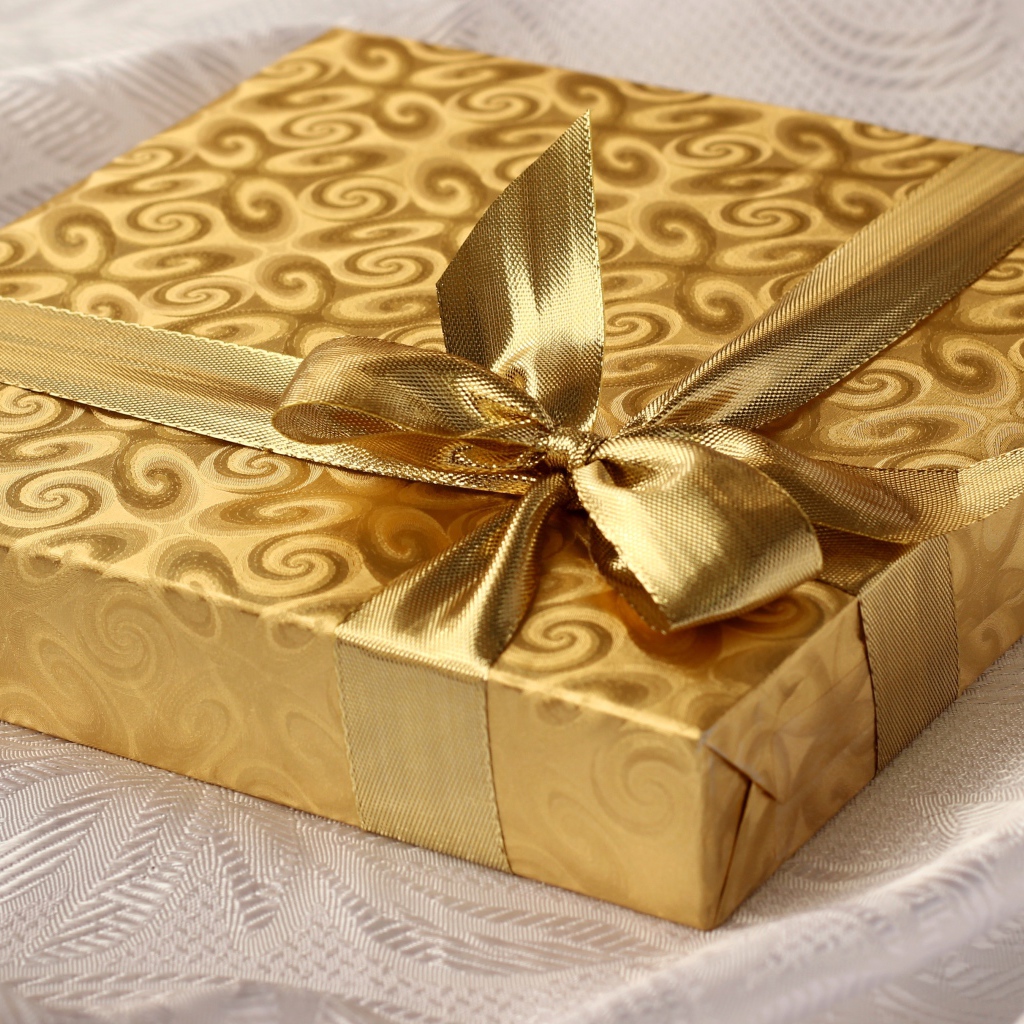 Красивая золотистая коробка с подарком на кровати 