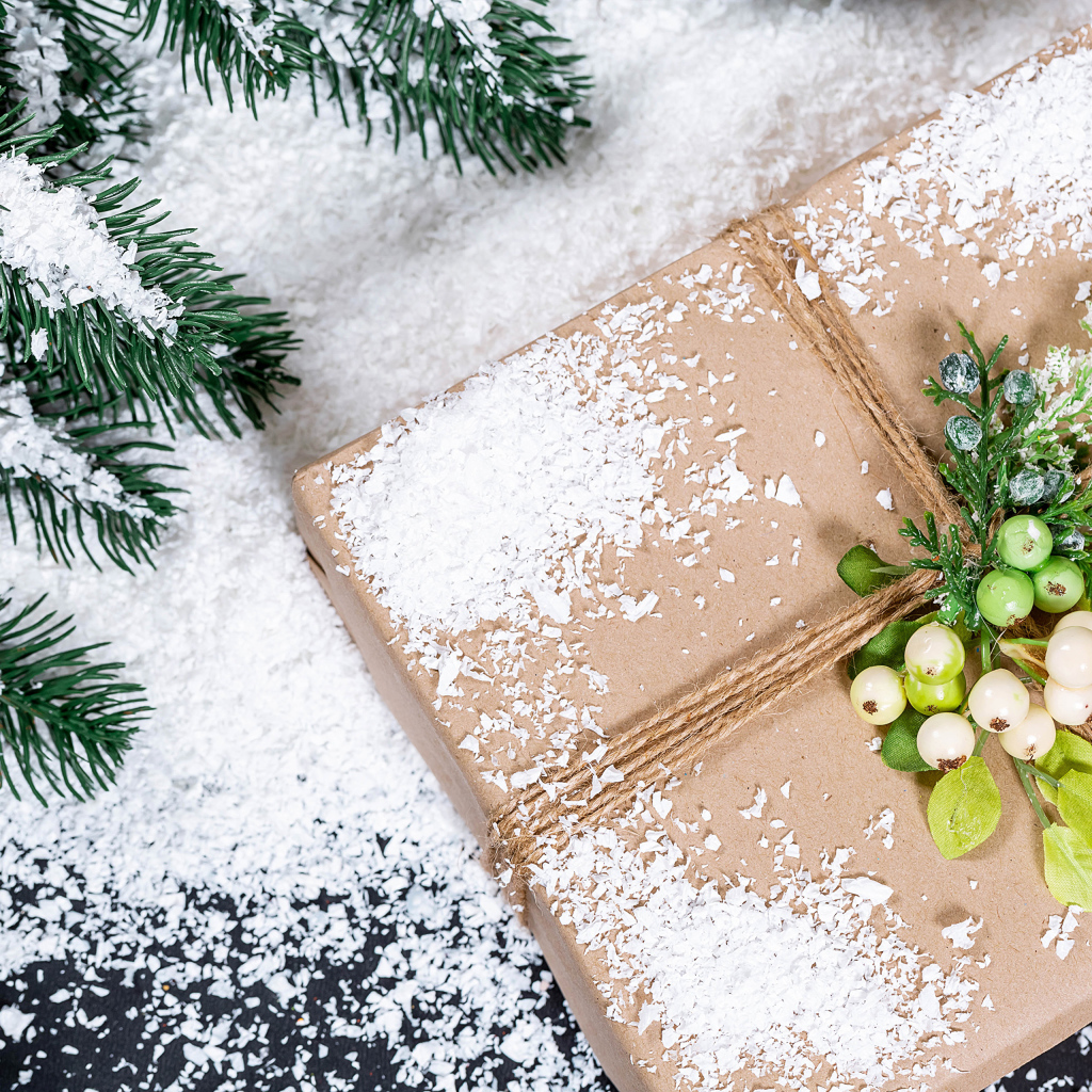 Подарок с заснеженной веткой ели на столе