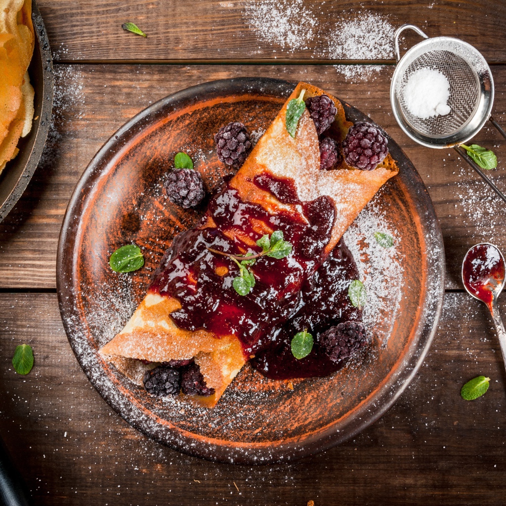 Блин с ягодами и джемом на тарелке с сахарной пудрой