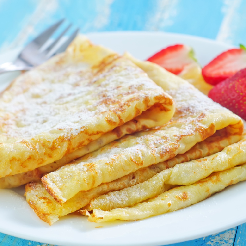 Румяные тонкие блинчики на тарелке с клубникой 