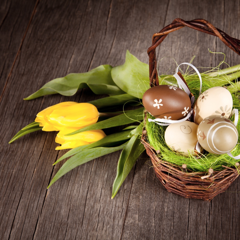 Маленькая корзина с пасхальными  яйцами на столе с тюльпанами