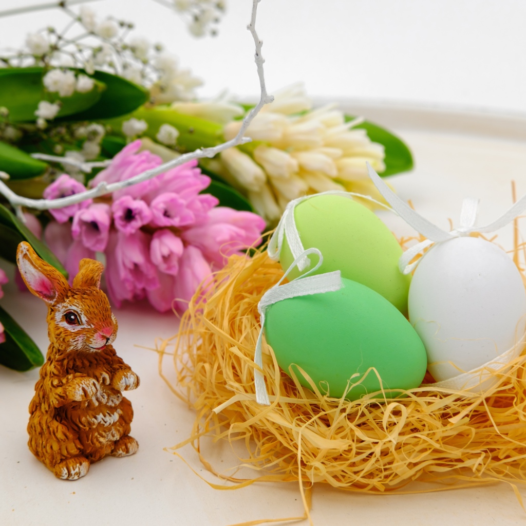 Три пасхальных яйца в гнезде на столе с цветами