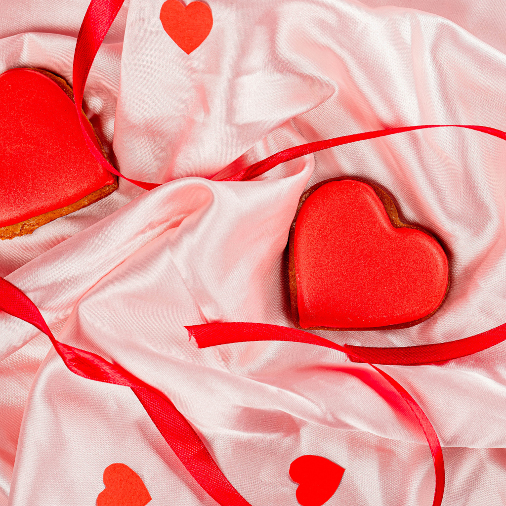 Два красных сердечка с ленточкой на розовой ткани на день влюбленных
