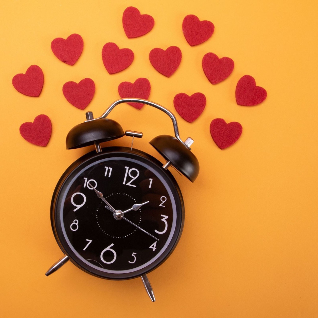 Черный будильник с сердечками на оранжевом фоне