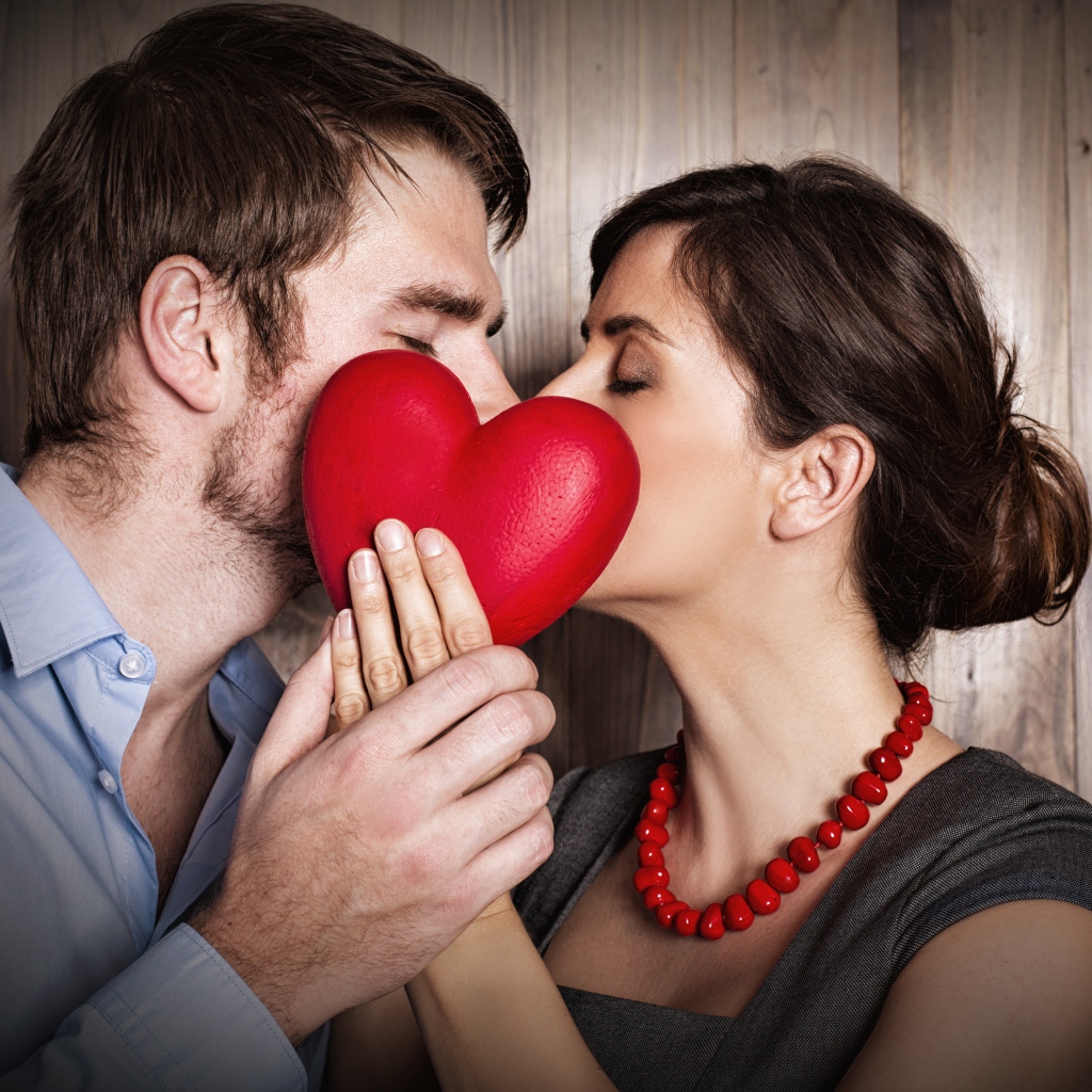Kiss of a couple in love behind a red heart
