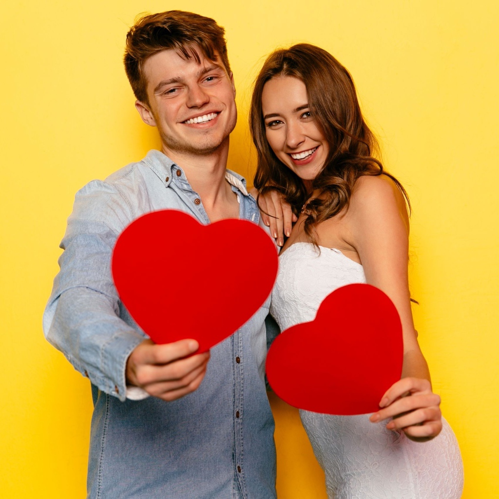 Влюбленная пара на желтом фоне с бумажными сердечками в руках 