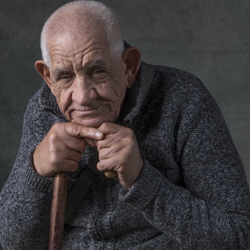 Пожилой мужчина в теплом свитере на сером фоне 