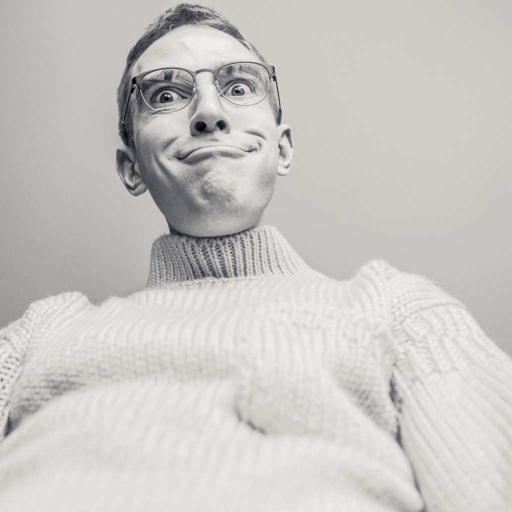 Мужчина в очках корчит лицо на сером фоне