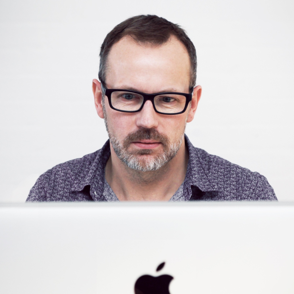 Серьезный мужчина в очках сидит за макбуком