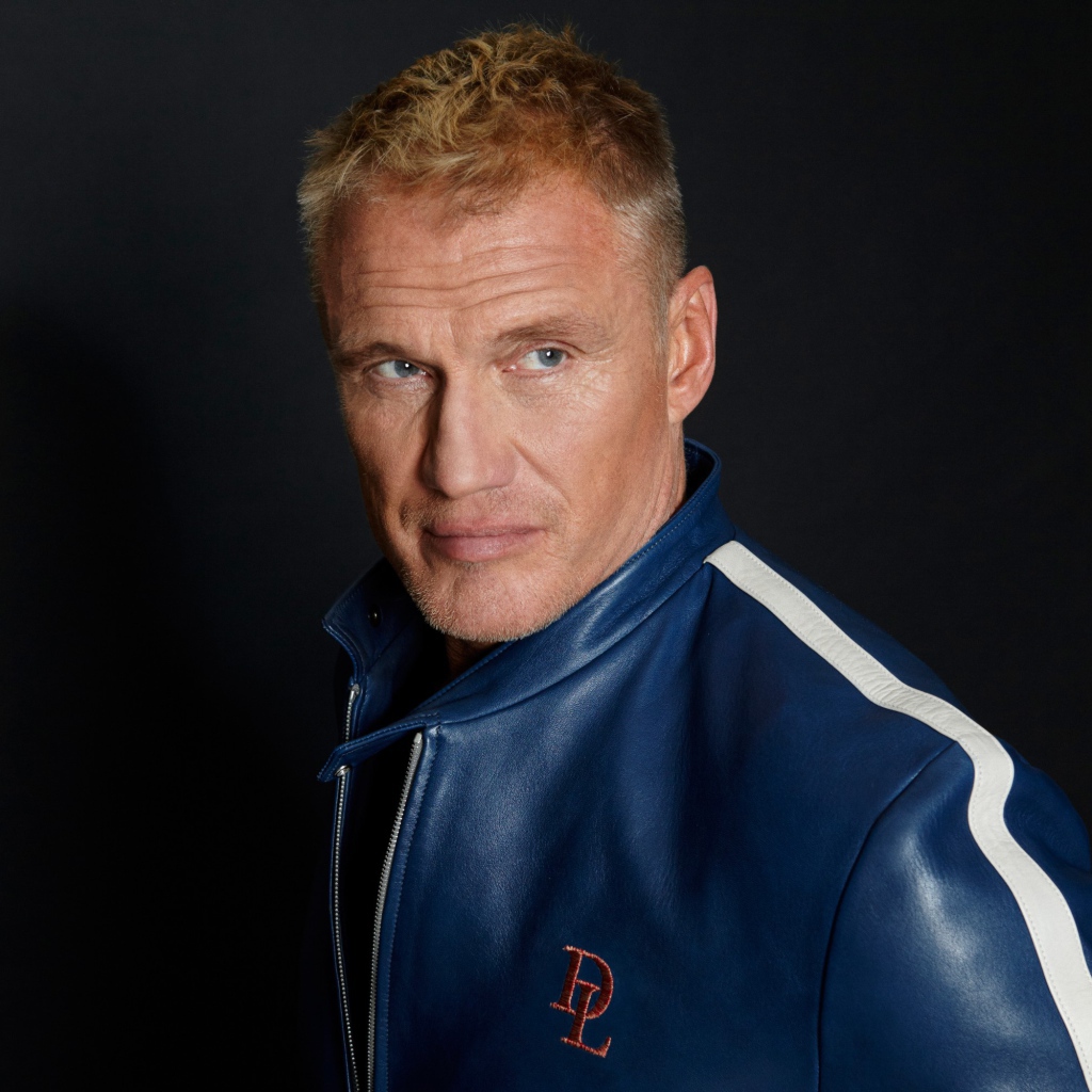 Актер Дольф Лундгрен в куртке на фоне  серой стены