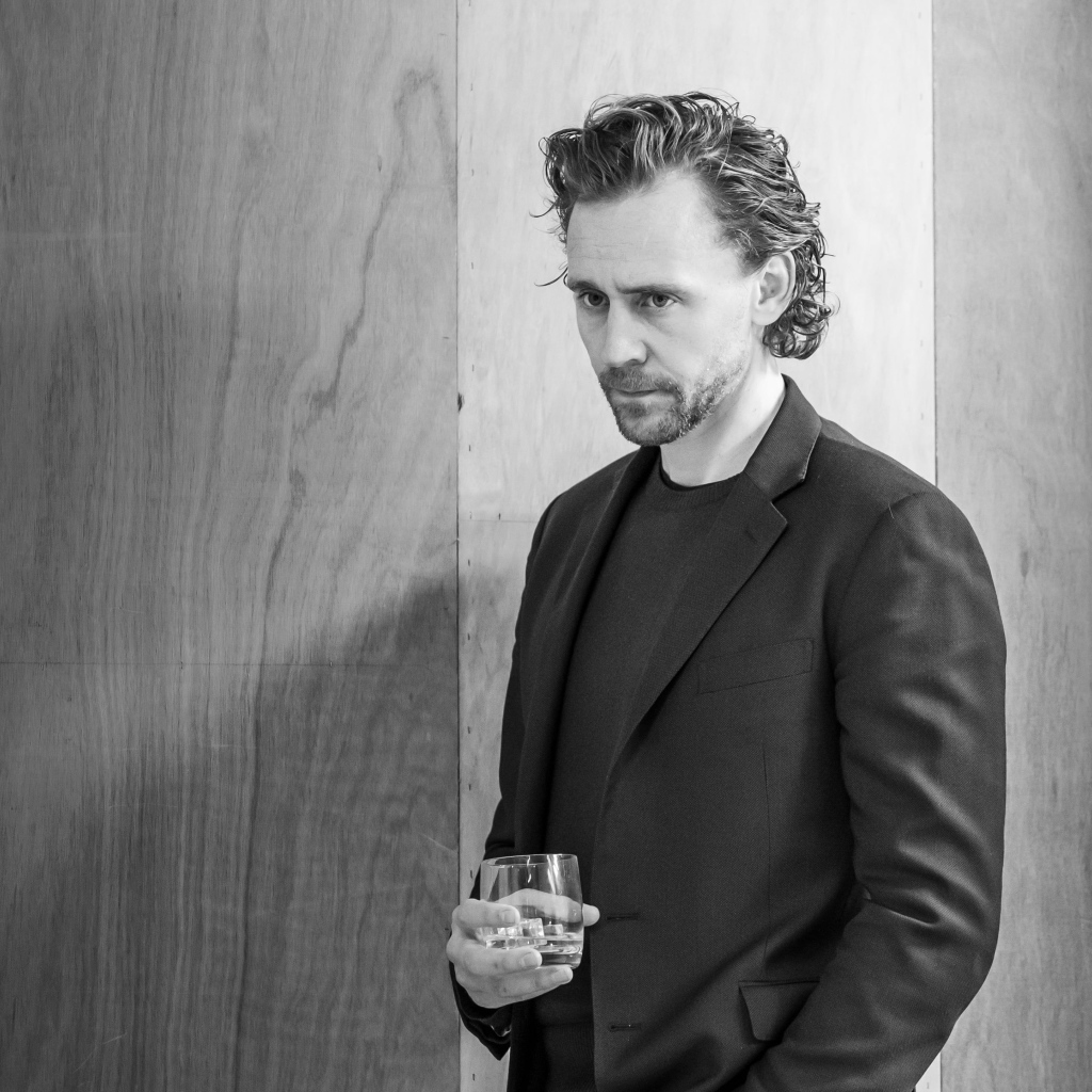 Актер Том Хиддлстон с бокалом в руке на фоне стены