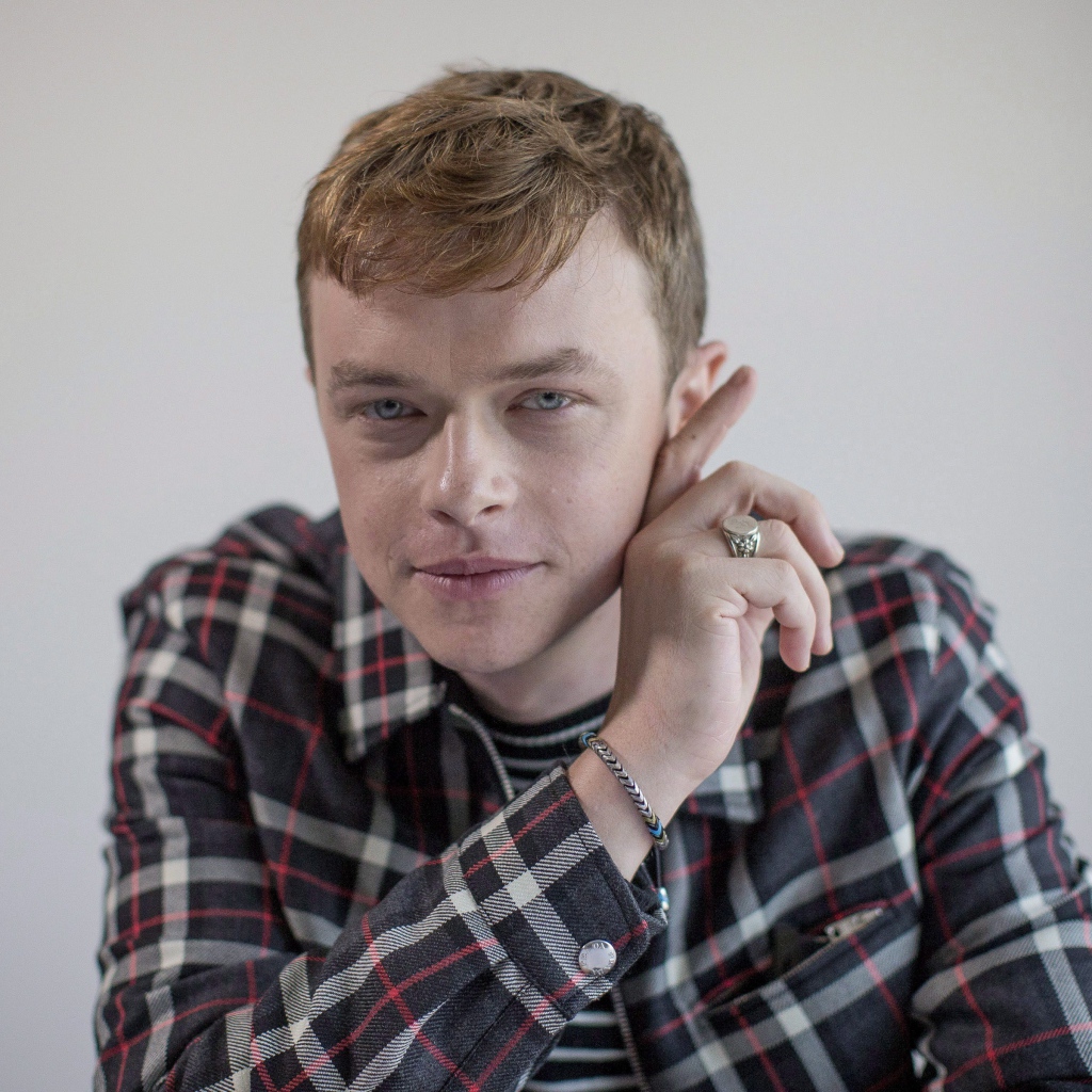 Молодой актер Дэйн Дехаан в рубашке на сером фоне