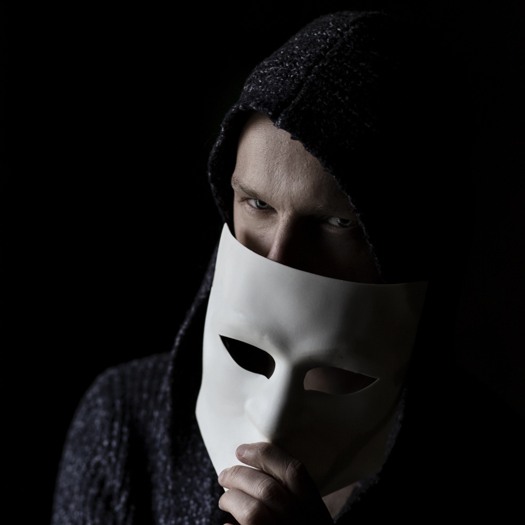 Мужчина прикрывает лицо белой маской на черном фоне