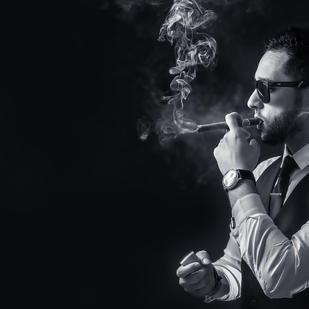 Мужчина с сигарой в руке на черном фоне 