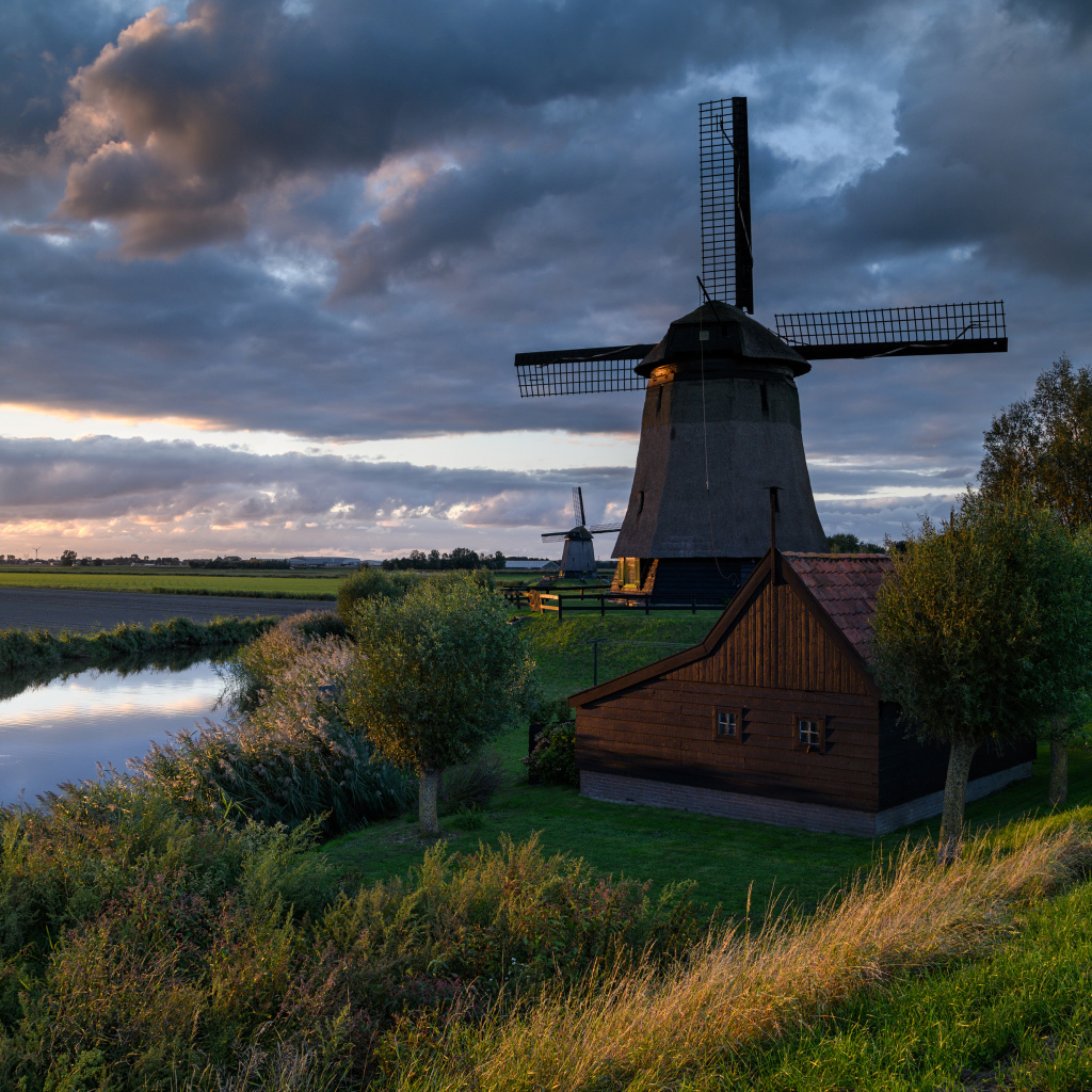 Большая ветряная мельница у реки на закате