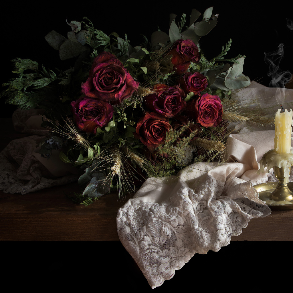 Завядший букет роз со свечой на столе