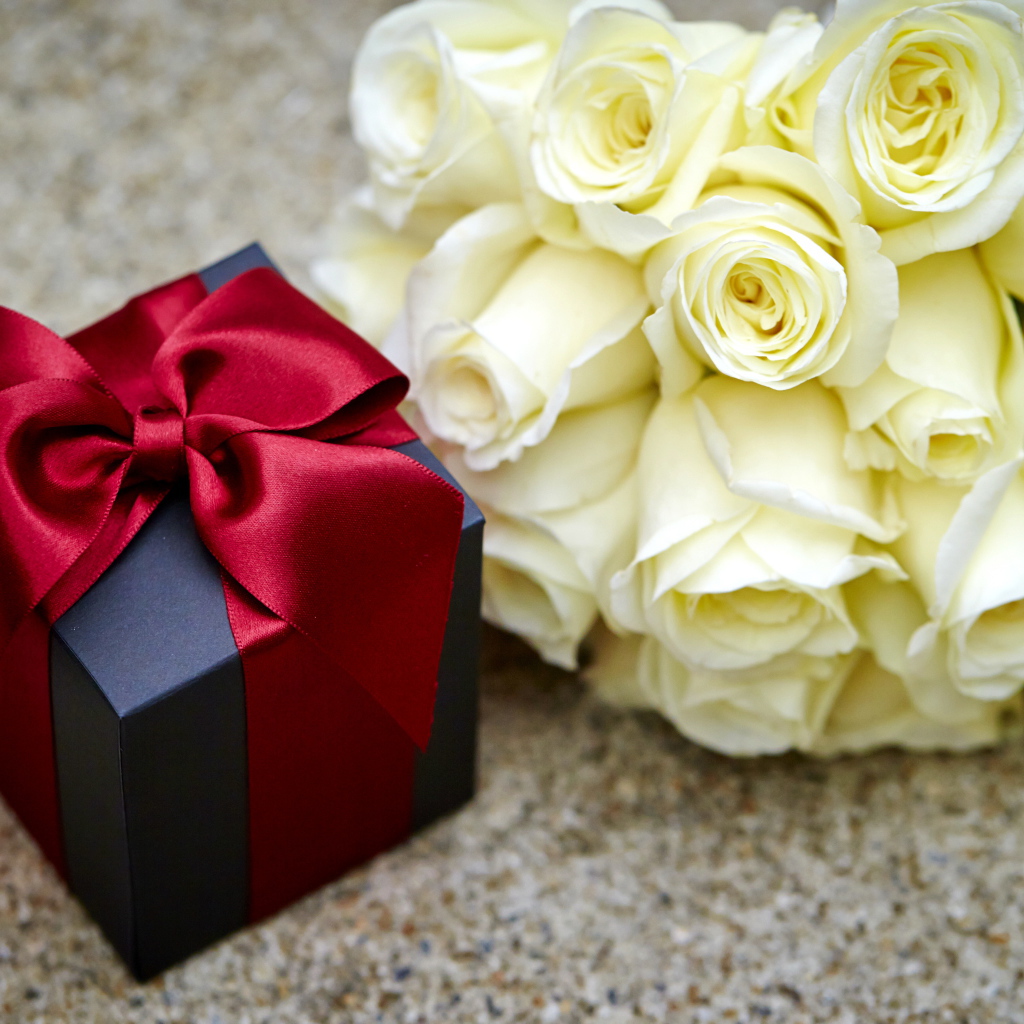 Букет белых роз с черным подарком на столе