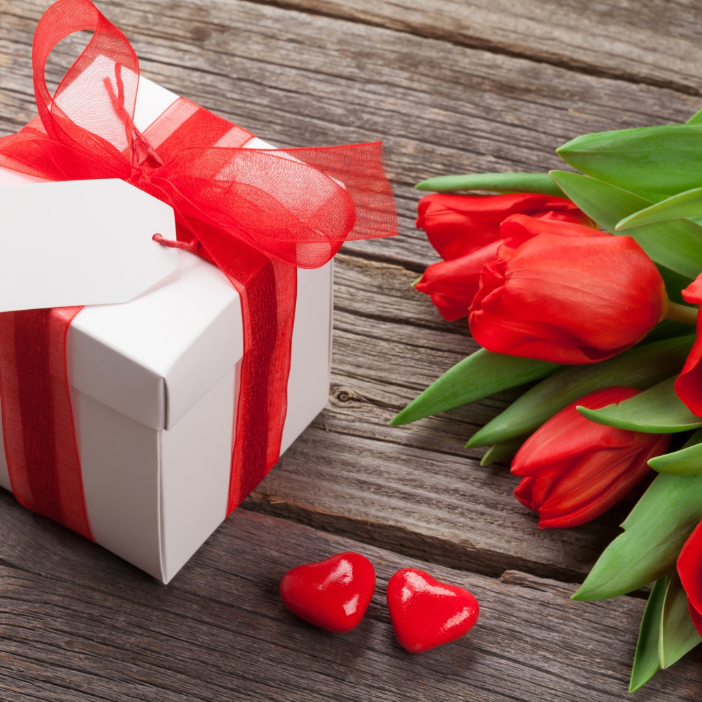 Red tulips with a big gift on a wooden table