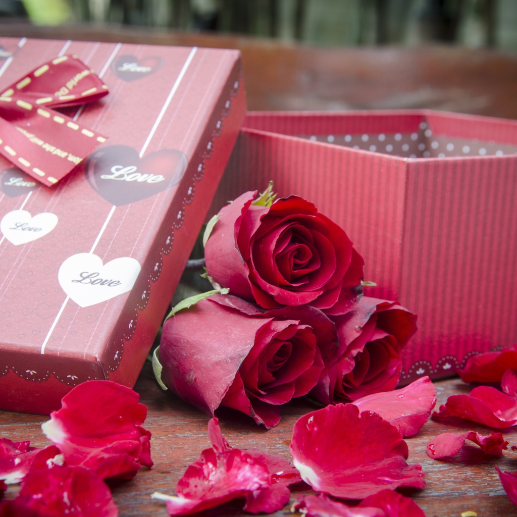 Три красные розы с лепестками  на столе с подарком