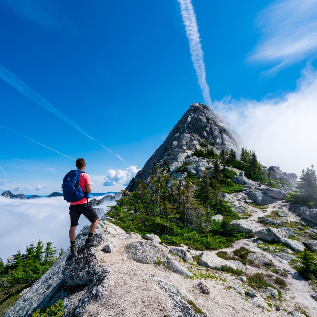 Мужчина подымается на вершина горы под голубым небом 